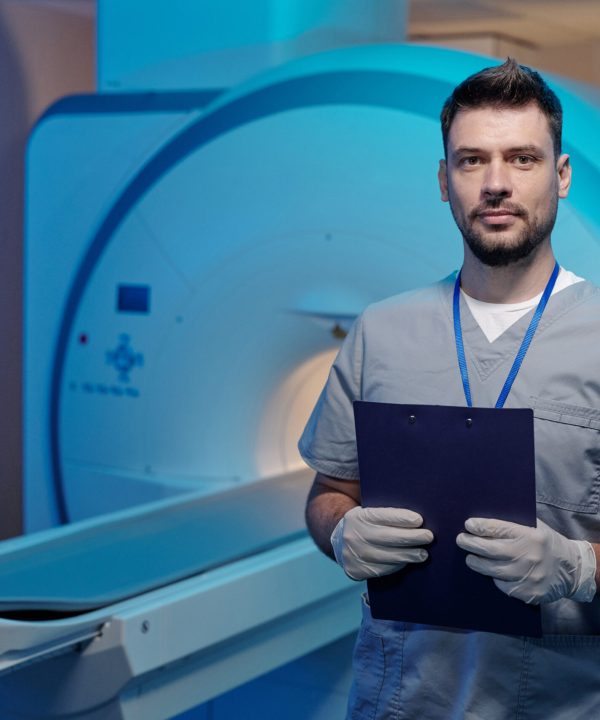 Young successful radiographer with document standing against mri scan machine